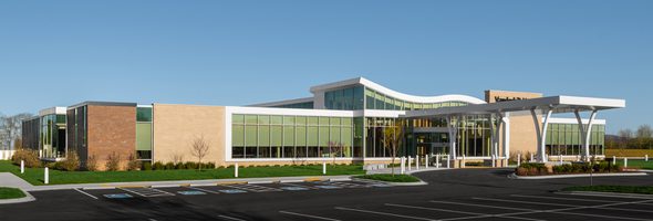 Exterior of building with glass facade, curved roof, and accessible parking in the foreground.